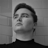 a black and white photo of Damien Pine, a pale man with shortish hair and a nice nose looking somewhat dramatically off into the distance because every time I smile in photos it looks like I'm going to bite someone and that's not the vibe I want to give off